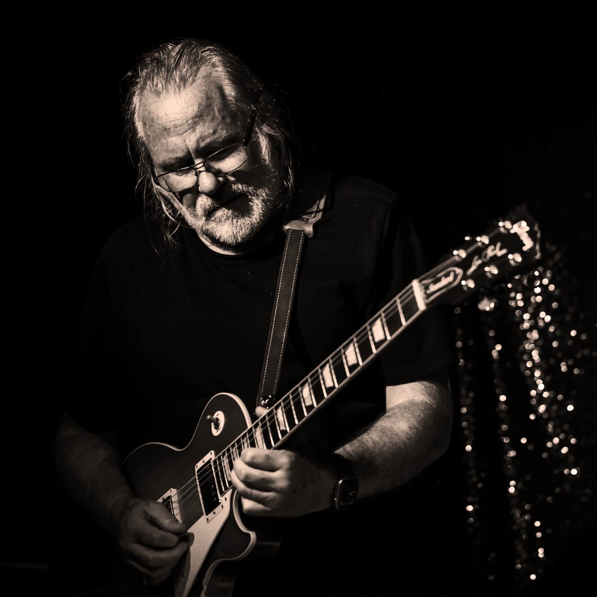 Man playing electric guitar in low light.