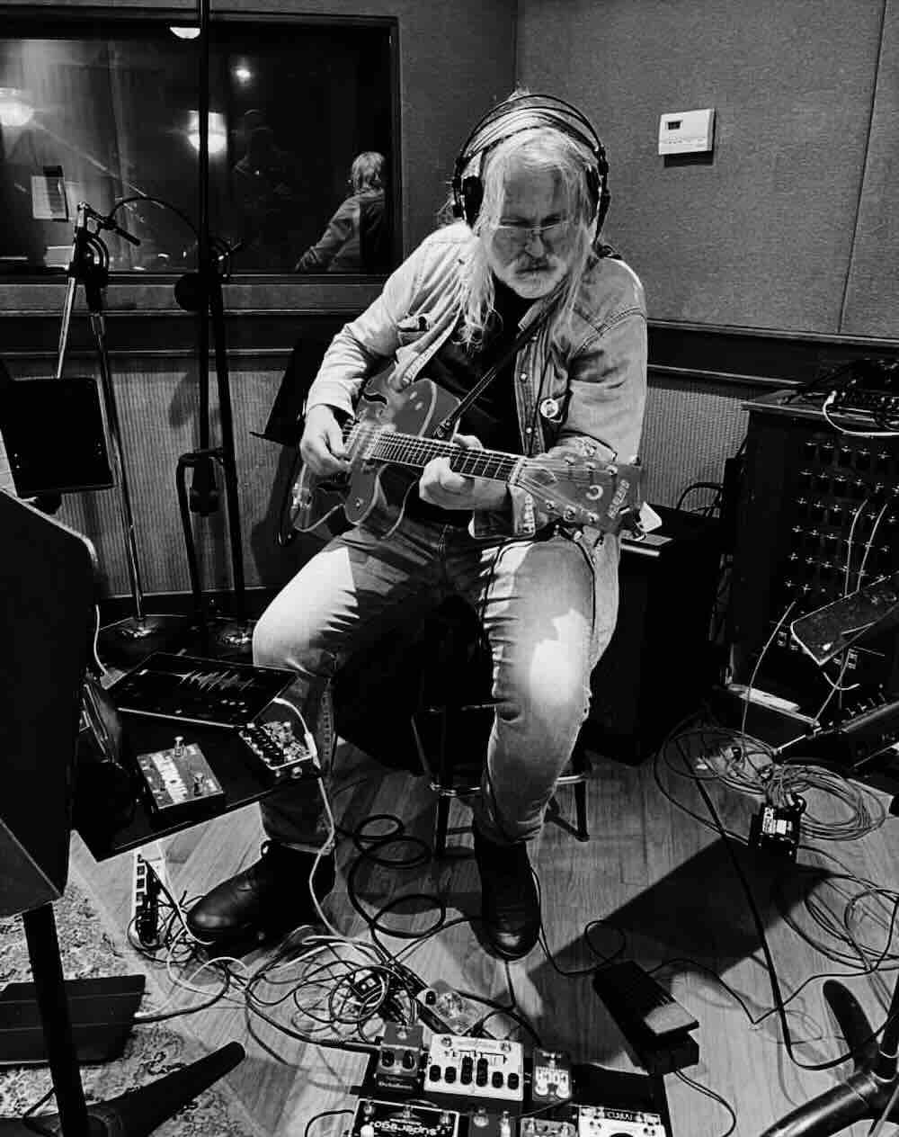 Musician playing guitar in recording studio with equipment.