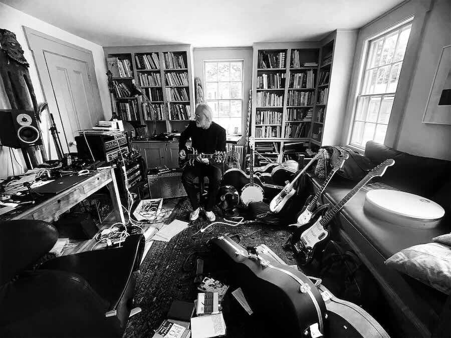 Musician playing guitar surrounded by other instruments.